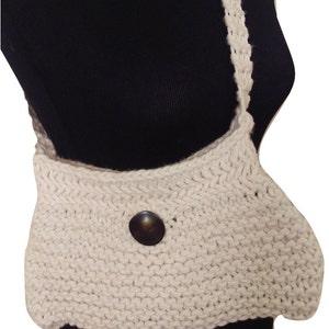 K&ouml;nnte beinhalten: Eine wei&szlig;e gestrickte Umh&auml;ngetasche mit braunem Knopfverschluss. Die Tasche ist aus dickem, strukturiertem Garn gefertigt und hat einen langen Riemen.
