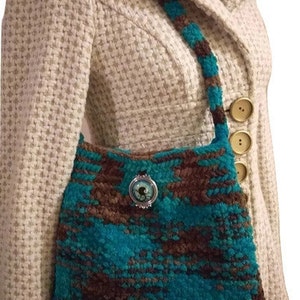 May include: A teal and brown crocheted handbag with a decorative button. The bag is worn over the shoulder of a person wearing a white tweed jacket.
