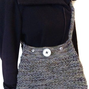 May include: A gray and green knitted crossbody bag with a single button closure. The bag is worn over a black coat with a fur collar.
