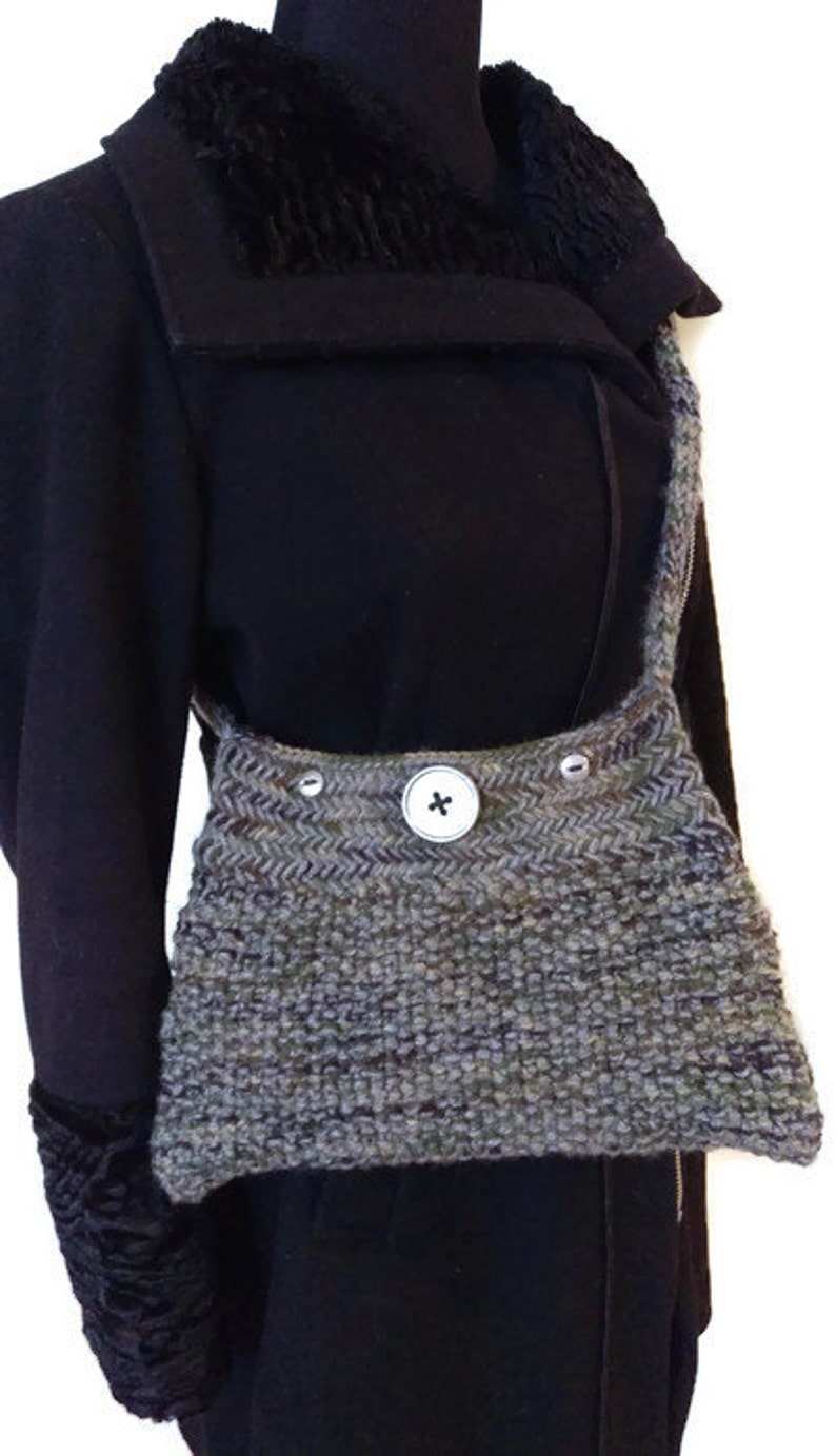 May include: A gray and green knitted crossbody bag with a single button closure. The bag is worn over a black coat with a fur collar.