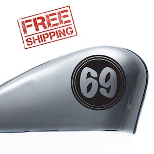 Puede incluir: Un tanque de gasolina de motocicleta plateado con una pegatina circular negra que dice "69" en una fuente retro.