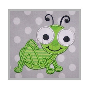 May include: Green embroidered grasshopper with large eyes and a smiling mouth on a gray background with white polka dots.