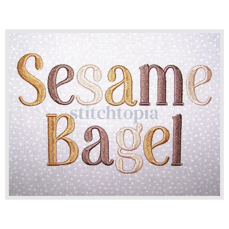 May include: Embroidered text on a white background with a subtle polka dot pattern. The words "Sesame Bagel" are displayed in a mix of gold, brown, and beige thread. The text is in a decorative, stylized font.