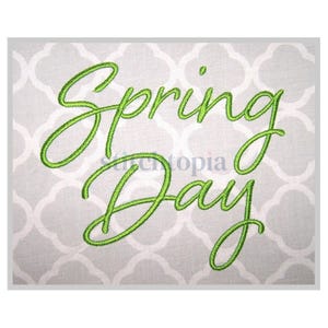 Op de afbeelding: Groene geborduurde tekst op een witte achtergrond met de tekst "Spring Day".