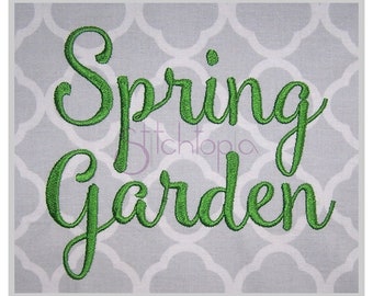 May include: Embroidered sign with the words "Spring Garden" in bright green script. The text is on a gray and white patterned background, framed by a white border. The design is likely for home decor.