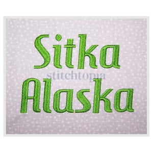 May include: A light gray fabric with a white polka dot pattern. The words "Sitka Alaska" are embroidered in bright green thread. The word "stitchtopia" is printed in gray between the words.