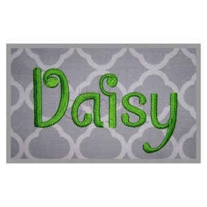 May include: A rectangular gray fabric with a white quatrefoil pattern. The name "Daisy" is embroidered in bright green, stylized script across the center. The embroidery has a textured, raised appearance.