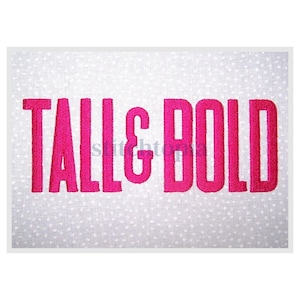 May include: Embroidered text on a white background with small white polka dots. The text reads "TALL & BOLD" in a bright pink color. The letters are thick and stand out against the background.