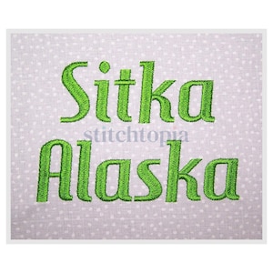 May include: A light gray fabric with a white polka dot pattern. The word "Sitka" is embroidered in green above "Alaska". The text "stitchtopia" is in the center. The embroidery has a textured appearance.