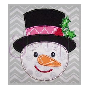 May include: A white snowman face with black eyes, a red mouth, and an orange carrot nose. The snowman is wearing a black top hat with a pink and white patterned band and a green holly sprig.