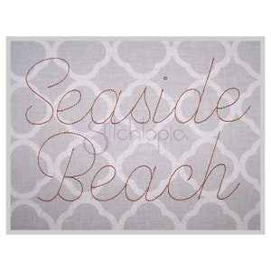 Puede incluir: Un letrero decorativo con las palabras "Seaside Beach" bordadas en fuente cursiva marrón. El fondo presenta un patrón de cuatro hojas gris y blanco. La palabra "Stichlopia" también es visible en una fuente más pequeña.