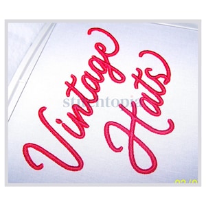 Peut inclure: Texte brodé en rouge sur tissu blanc : "Vintage Hats" en écriture cursive. La broderie est détaillée, les lettres se chevauchent légèrement. L'image est encadrée d'un bord blanc.