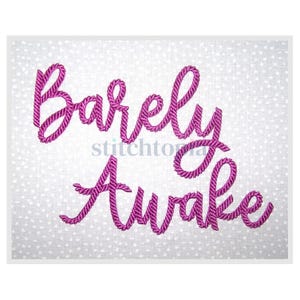 May include: A white fabric with a subtle polka dot pattern, embroidered with the words "Barely Awake" in a vibrant magenta color. The text is in a cursive style, giving it a handcrafted appearance. The image has a clean, minimalist aesthetic.