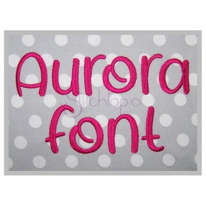 May include: A pink "Aurora Font" embroidery design on a grey background with white polka dots.