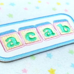 May include: A white patch with a blue border featuring four colorful blocks spelling out "ACAB".