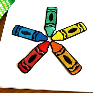 Op de afbeelding: Zes kleurrijke waskrijt-patches in de vorm van een ster. De waskrijtjes zijn rood, oranje, geel, groen, blauw en paars.