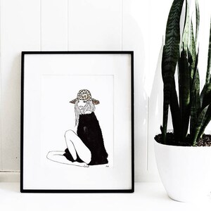 May include: Black and white line drawing of a woman wearing a leopard print hat and a black sweater. The drawing is framed in a black frame and is hanging on a white wall.