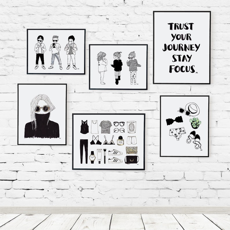 May include: A white brick wall with black framed prints. The prints feature illustrations of people, clothing, and text. One print says "Trust your journey stay focus".