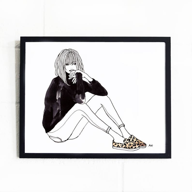 May include: Black and white line drawing of a woman sitting with her legs crossed, wearing a black turtleneck sweater, jeans, and leopard print slip-on shoes. The drawing is framed in a black frame.