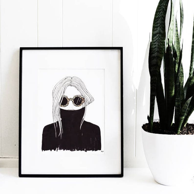 May include: Black and white line drawing of a person wearing a black turtleneck sweater and round sunglasses. The drawing is framed in a black frame and is hanging on a white wall.