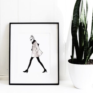Pu&ograve; includere: Illustrazione in bianco e nero di una donna che indossa un cappotto, occhiali da sole e uno chignon. L'illustrazione &egrave; incorniciata in una cornice nera e appesa a un muro bianco.