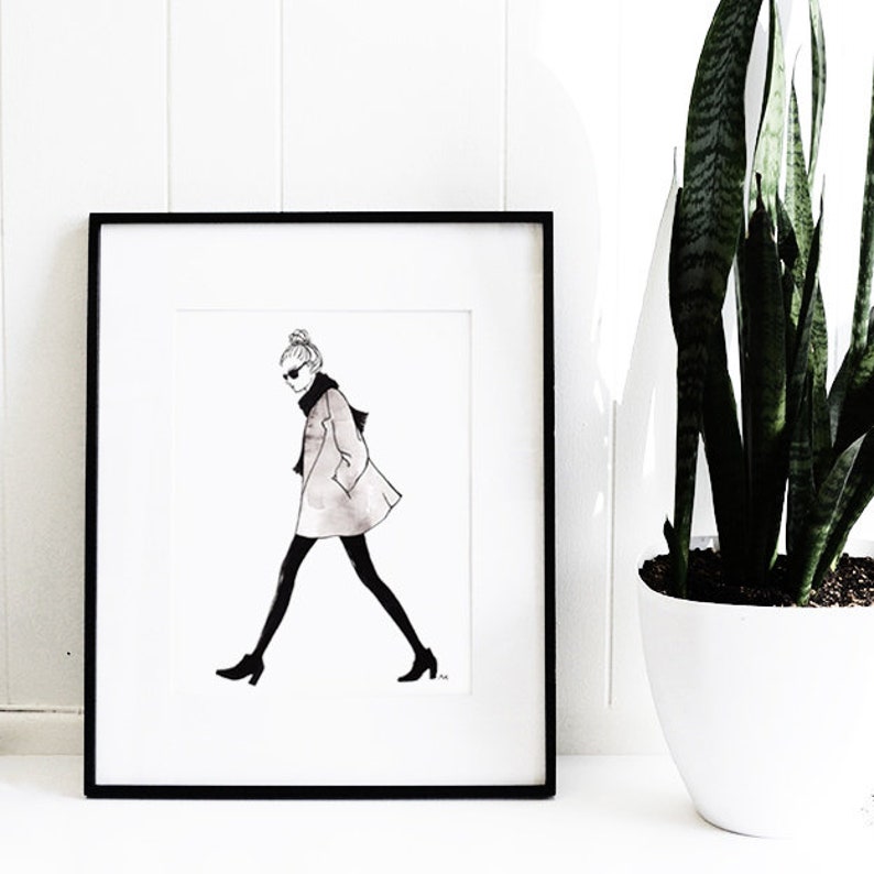 Pu&ograve; includere: Illustrazione in bianco e nero di una donna che indossa un cappotto, occhiali da sole e uno chignon. L'illustrazione &egrave; incorniciata in una cornice nera e appesa a un muro bianco.