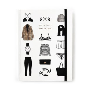 May include: A white notebook with a black elastic band closure. The cover features black and white illustrations of various clothing items, including a leopard print coat, a striped shirt, a pair of sunglasses, and a black handbag. The text "MINIMALIST NOTEBOOK" is printed in gold on the cover.