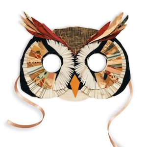 May include: A brown, black and white owl mask with a red and orange beak. The mask is made of paper and fabric and has a brown ribbon attached.