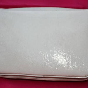 May include: A white leather shoulder bag with a flap closure and a silver buckle. The bag has a smooth, glossy finish.