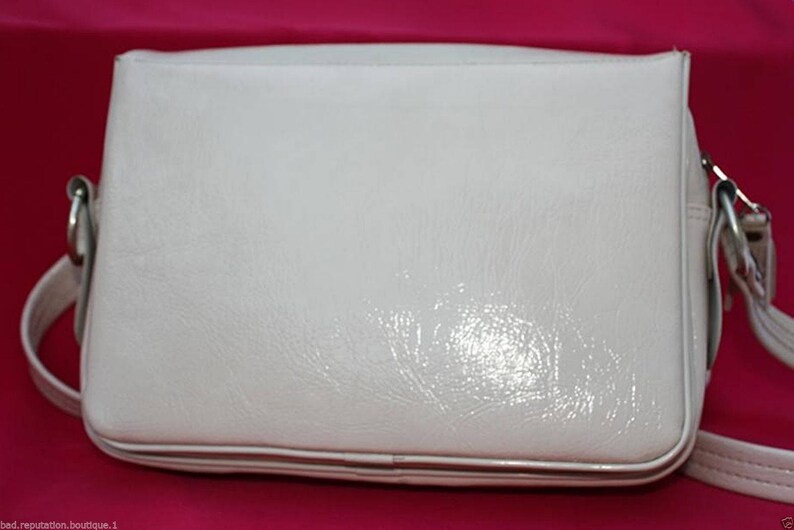 May include: A white leather shoulder bag with a flap closure and a silver buckle. The bag has a smooth, glossy finish.