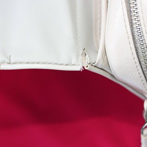 May include: Close-up of a white leather handbag with a zip closure. The zip is silver and the bag has a white lining.