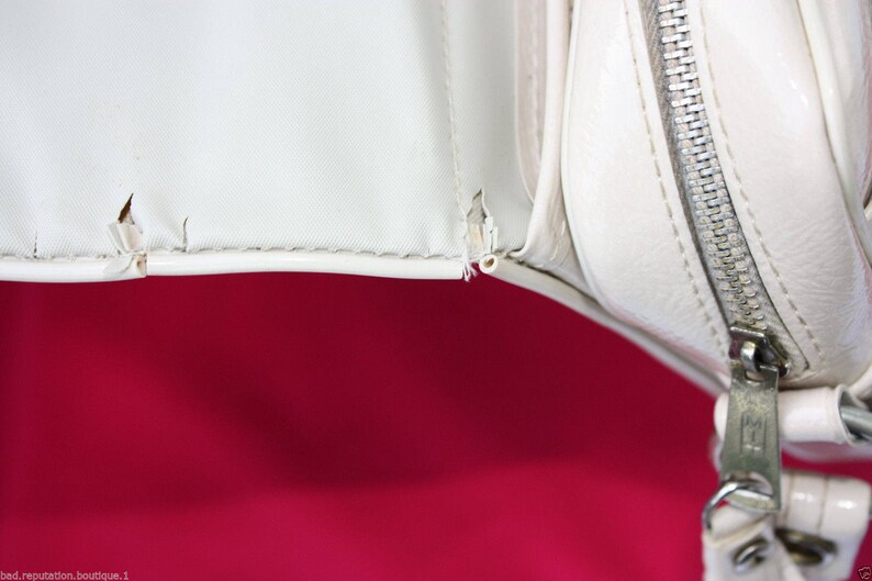 May include: Close-up of a white leather handbag with a zip closure. The zip is silver and the bag has a white lining.