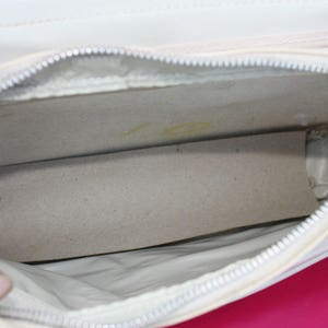 May include: White leather handbag with a zip closure and a white fabric lining. The bag is open and the lining is visible.