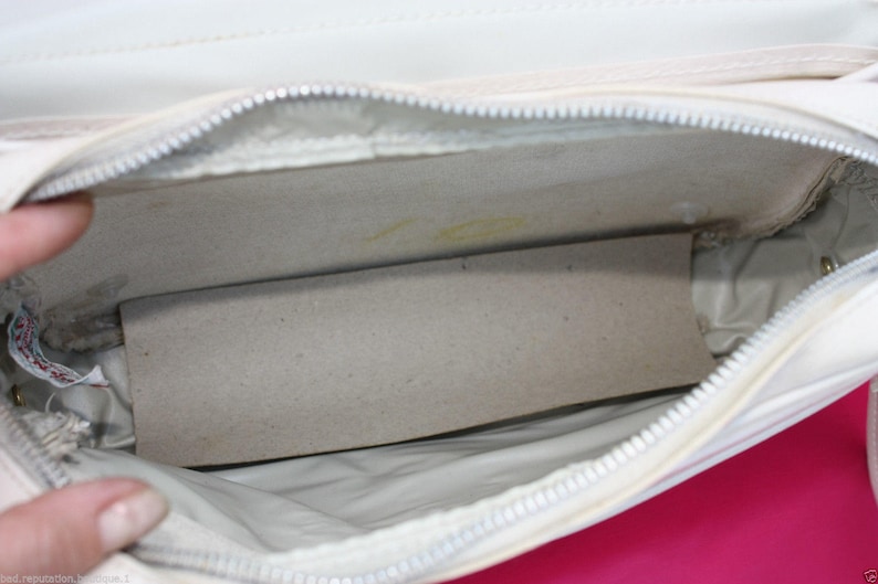 May include: White leather handbag with a zip closure and a white fabric lining. The bag is open and the lining is visible.