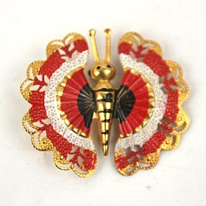 May include: A gold-tone butterfly brooch with red, white, and black enamel wings. The wings have a scalloped edge and are decorated with a delicate pattern.