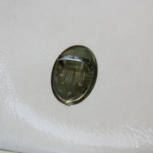 May include: A gold-coloured oval-shaped metal handle with a silver-coloured loop. The handle is attached to a surface.