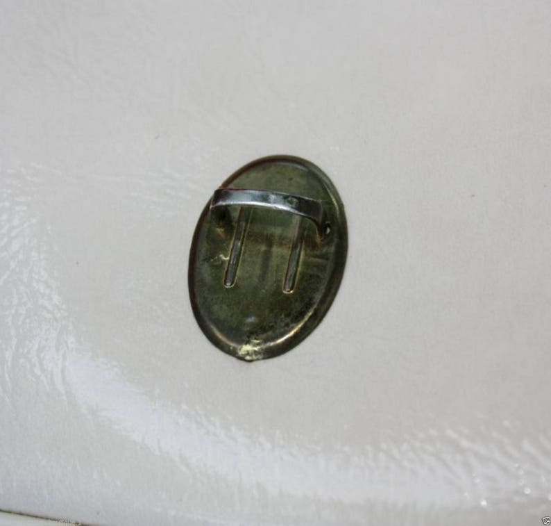 May include: A gold-coloured oval-shaped metal handle with a silver-coloured loop. The handle is attached to a surface.