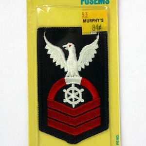 May include: A rectangular Joy-Patch iron-on fusem patch featuring a black background with an embroidered white eagle above a white ship's wheel and three red horizontal stripes. The packaging includes the text Joy-Patch, Iron-On Fusems, and Murphy's 84 cents.