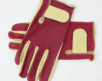 May include: A pair of leather gloves with a burgundy red palm and a light tan back. The gloves have a stitched seam around the wrist and a small leather tab on the back of the hand.