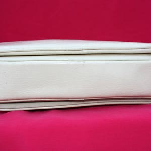 May include: A white leather handbag with a flap closure and a small tassel. The bag has a smooth, textured surface and a subtle sheen.
