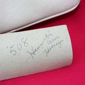 May include: A close-up of a white paper label with handwritten text that reads "508 Janine Anna Werneriger."
