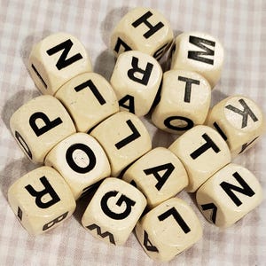 May include: A collection of off-white letter dice with black uppercase letters. The dice are scattered on a light-colored, checkered surface. The letters visible include P, O, R, L, A, T, G, N, H, M, and K.