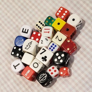 May include: A collection of assorted multi-colored dice featuring various designs, including standard pips, numbers, letters, a lightning bolt, a club symbol, and a Harley-Davidson logo. The dice are square-shaped and vary in size and color.