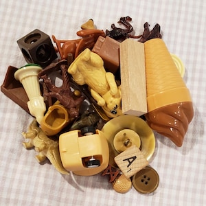 May include: A collection of small, colorful toys and objects, including a yellow bear, a brown cube, a light brown ice cream cone, and a wooden block. Other items include a button, a small toy car, and a wooden letter tile.