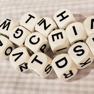 May include: A collection of ivory-colored dice with black letters and numbers. The dice are scattered on a light-colored, patterned surface. The letters and numbers are clearly visible, creating a playful and educational theme.