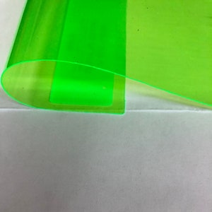 May include: A close-up of a translucent, neon green sheet with a curved edge. The sheet is layered over a lighter green section, creating a gradient effect. The background is a plain, off-white surface.