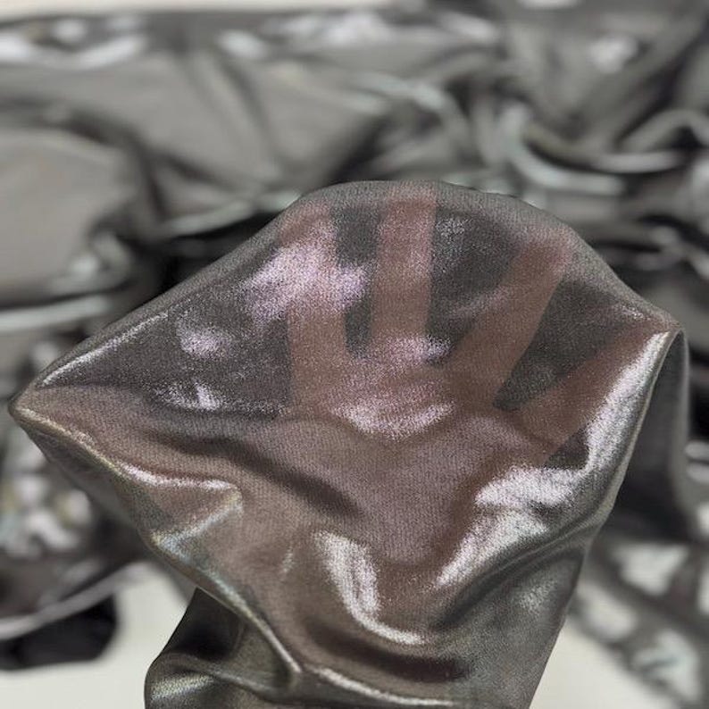 May include: Close-up of a shimmering, sheer fabric in shades of grey and silver. The fabric is draped and folded, creating a play of light and shadow. The material appears lightweight and delicate, with a subtle sheen.