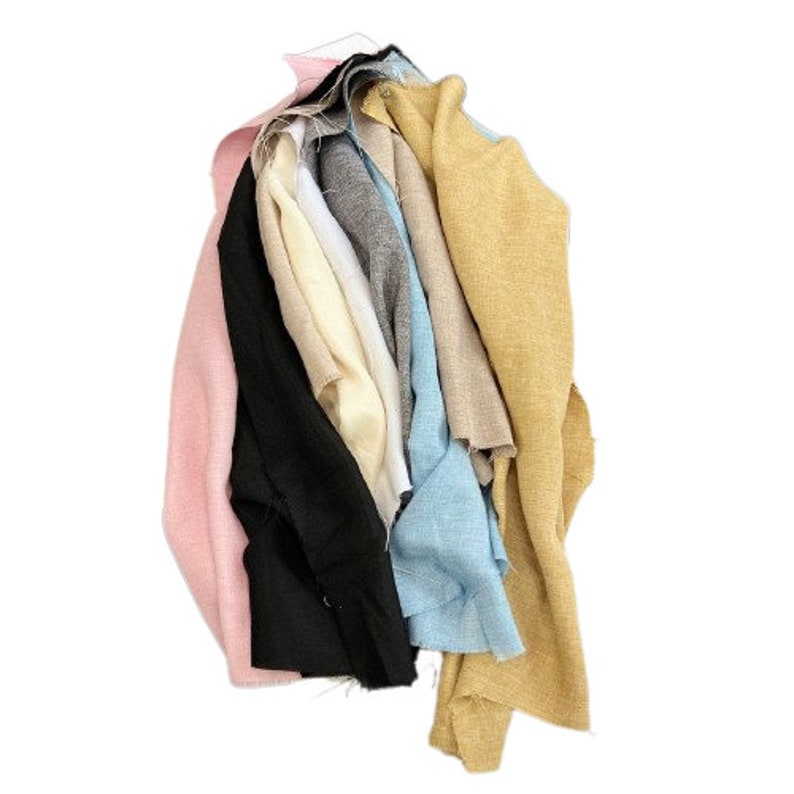 May include: A stack of fabric scraps in various colors, including pink, black, gray, beige, and blue. The fabric scraps are arranged in a pile, with the pink fabric scrap on the bottom and the blue fabric scrap on the top.