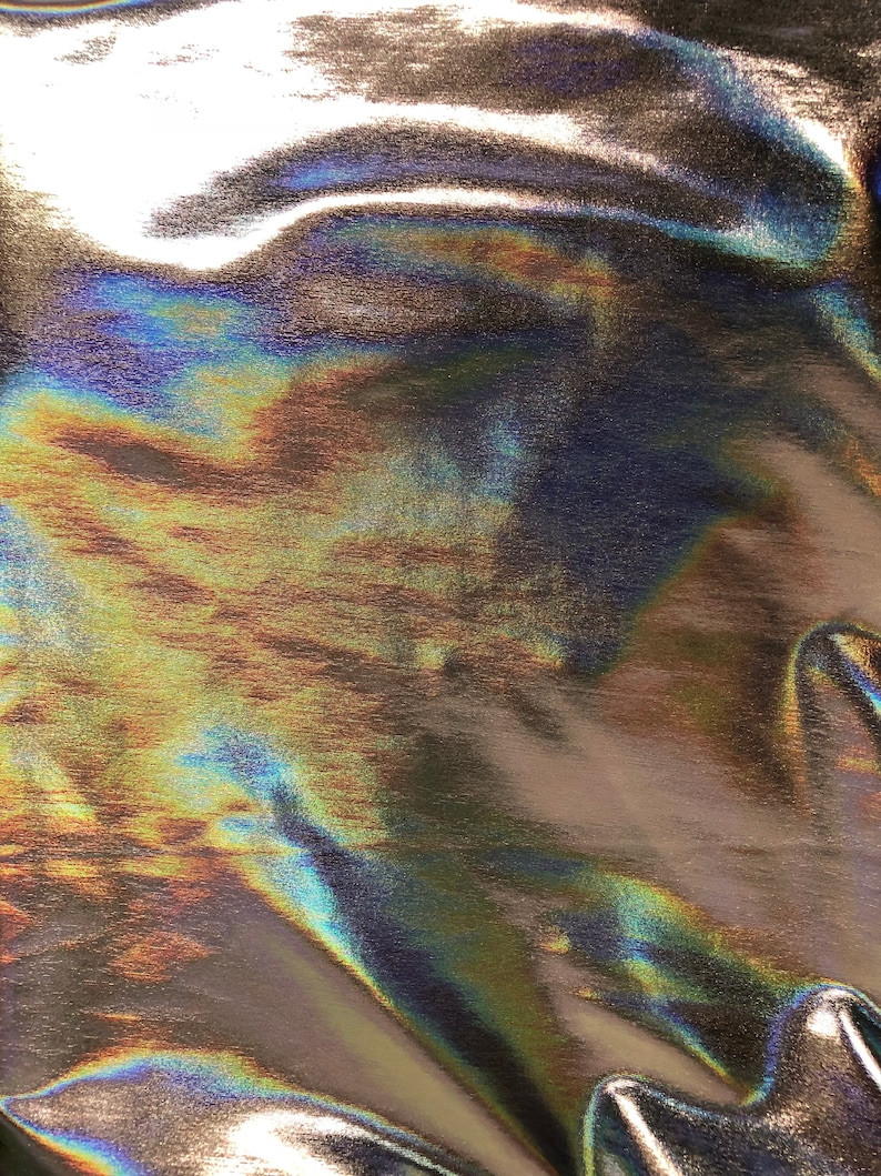 May include: Close-up of iridescent fabric with a metallic sheen. The fabric is wrinkled and has a textured surface. The colors are a mix of blue, green, and gold.