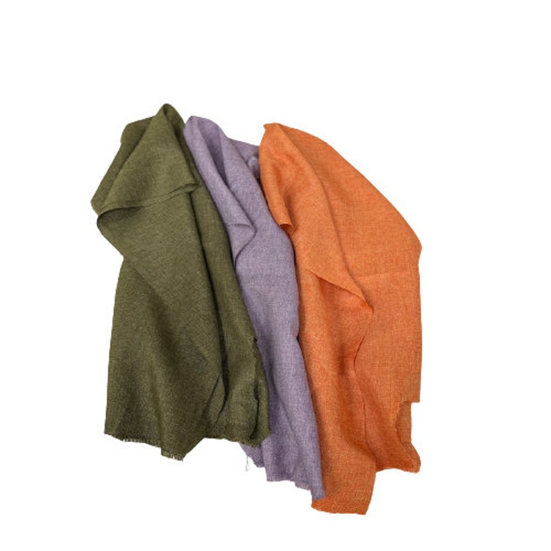 May include: Three fabric swatches in different colors: olive green, lavender, and orange. The swatches are folded and arranged in a stack.